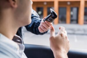 Close-up of a police officer administering a breathalyzer test to a driver sitting in a car, with the driver slightly out of focus in the foreground.